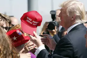 Presidente Donald Trump segurando um boné com o slogan “Make America Great Again” (Foto: Reprodução | AP Photo)