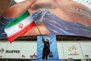 Mulher segura bandeira do Irã em frente à outdoor em Teerã que representa o presidente dos EUA, Donald Trump, e o fechamento do estreito de Hormuz (Foto: AFP - 5.mai.2026)
