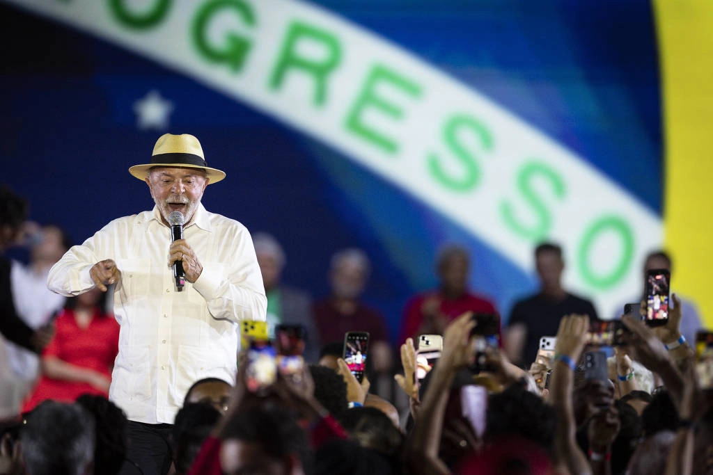 Homem de camisa branca e chapéu bege segura microfone e fala para público que registra com celulares. Ao fundo, parte da bandeira do Brasil com a palavra 'PROGRESSO'. Convenção nacional do Partido dos Trabalhadores (PT) que oficializa a candidatura do presidente Luiz Inácio Lula da Silva à reeleição para a Presidência da República
